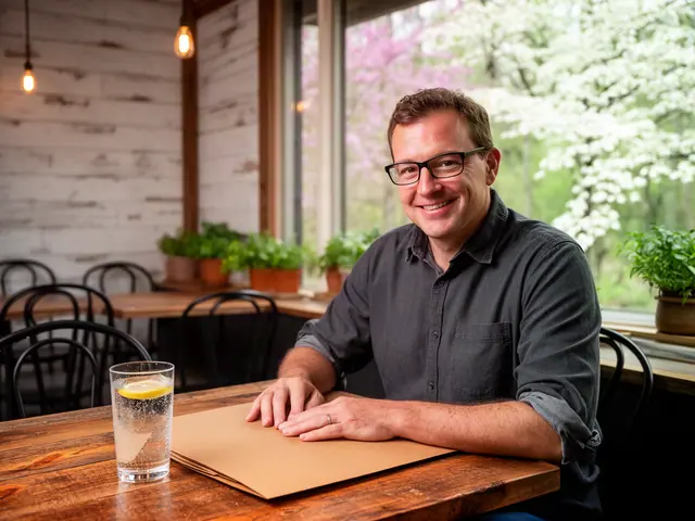 Smiling cafe owner in glasses sits at a rustic table with a kraft folder and glass of lemon water